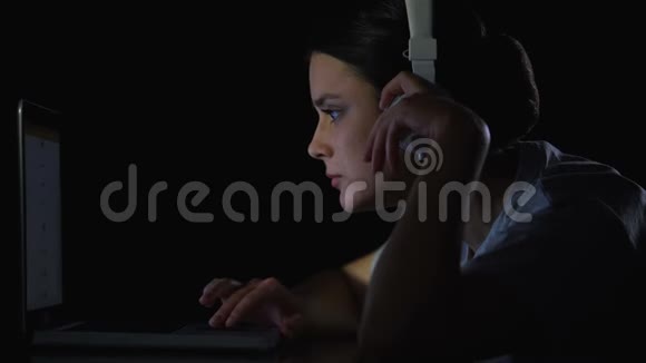 年轻女孩听着耳机里的音乐在笔记本电脑上滚动社交网络视频的预览图