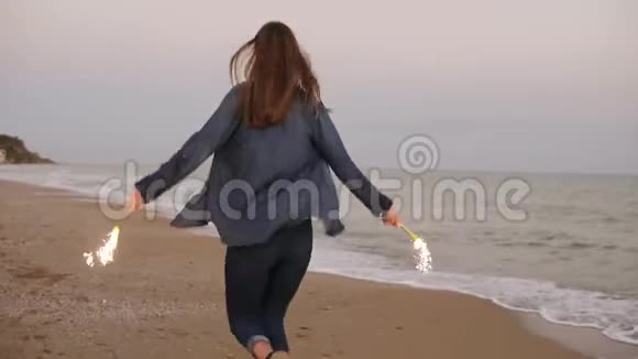 日落时分年轻迷人的女子在海边奔跑双手拿着燃烧的闪闪发光的蜡烛视频的预览图