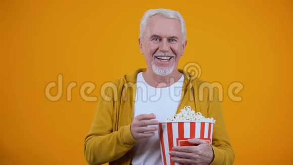 在看电影的时候头发花白的男人一边吃爆米花一边笑视频的预览图