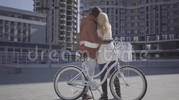 一对年轻幸福的情侣在爱中微笑着与自行车交流的肖像站在一辆自行车的背景上视频的预览图