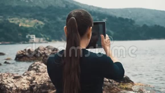女游客站在海滩上在石板岩石和树木上拍照视频的预览图