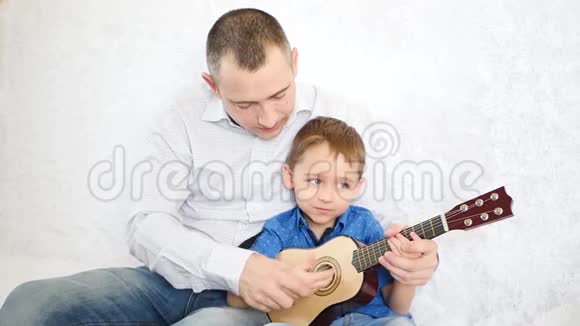 一位父亲拥抱他的儿子教他弹吉他幸福家庭的概念视频的预览图