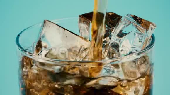 在青色背景下将可乐或棕色软饮料倒入装满冰块的玻璃杯中特写慢镜头继续拍摄视频的预览图