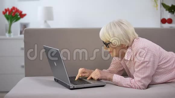 快乐的老太太在家里打手提电脑为老年人工作自由职业视频的预览图