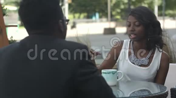 拿着一杯咖啡的黑人女孩和她的美国黑人同事交谈坐在咖啡馆外面视频的预览图