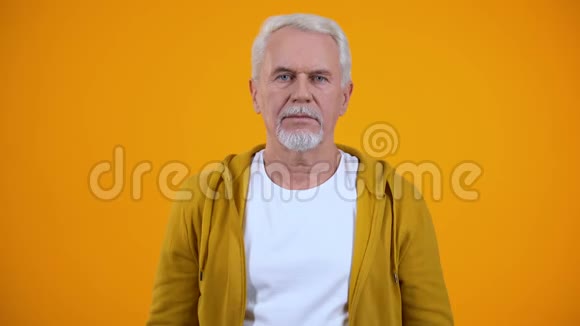 灰发养老金领取者在橙色背景下表现出沉默秘密视频的预览图