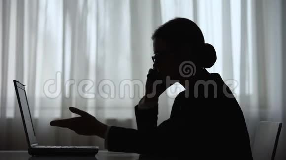 女商人在晚上打电话在笔记本电脑上做笔记的黑暗轮廓视频的预览图