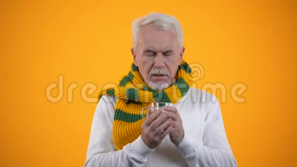 患病的老年男性围着围巾喝热饮料减少流感症状视频的预览图