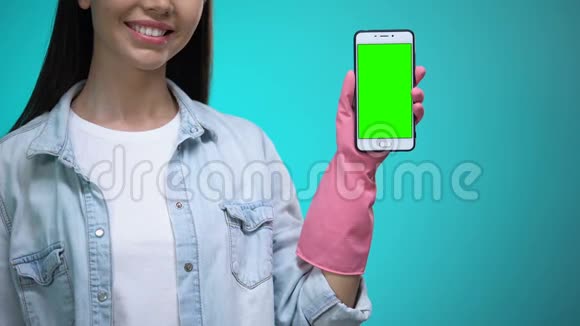 戴着手套的微笑女人拿着绿色屏幕的智能手机提供清洁服务视频的预览图