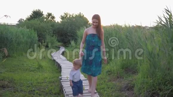 一家人走在大自然中年轻快乐的母亲牵着小儿子的手走在草地上的独木桥上视频的预览图
