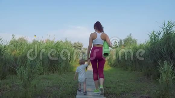 运动家庭年幼的运动妈妈带着孩子在绿色植被中练习后走在大自然的桥上视频的预览图