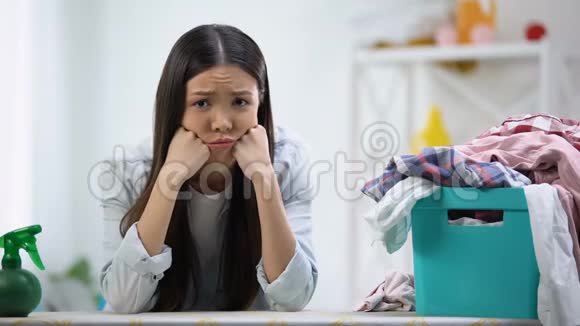 心烦意乱的家庭主妇看着相机桌子上装满衣服的洗衣篮视频的预览图