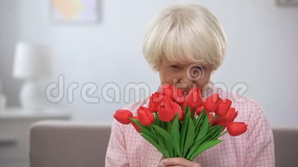 快乐的老妇人嗅着郁金香对着镜头微笑母亲节视频的预览图