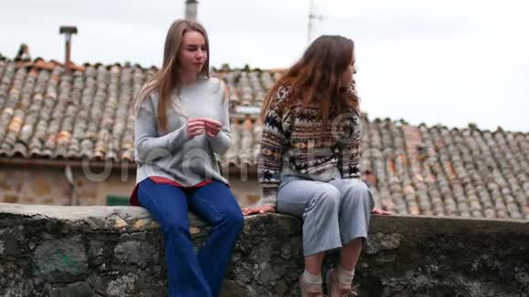 两个年轻的女人坐在水泥的窗台上环顾四周视频的预览图