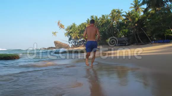 令人兴奋的赤脚男子在蓝天下沿着海岸线奔跑视频的预览图