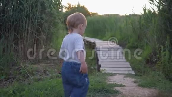 童年时快乐的小男孩光着脚走在大自然的木桥上在绿草中视频的预览图