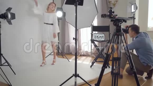拍摄的后台专业摄影师拍摄在白色背景上摆姿势的可爱女人的照片视频的预览图