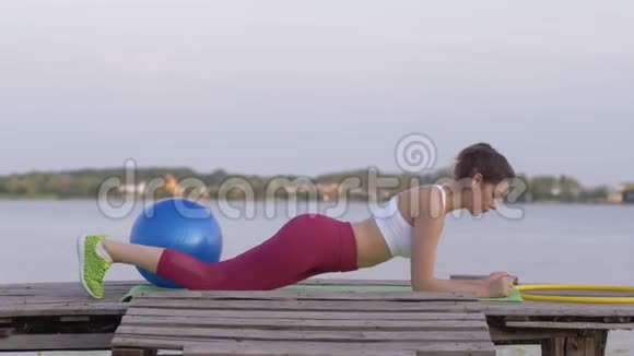穿着运动训练服在大自然桥上做木板运动的强壮美丽的健身女子视频的预览图