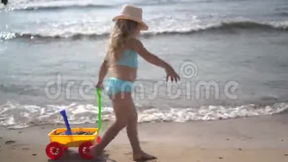 穿着泳衣的赤脚小女孩喜欢在沙滩上玩玩具推车视频的预览图