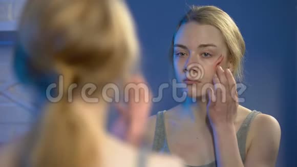 恐怖的年轻女子用遮瑕膏遮住脸上的伤口在家中的镜子前视频的预览图