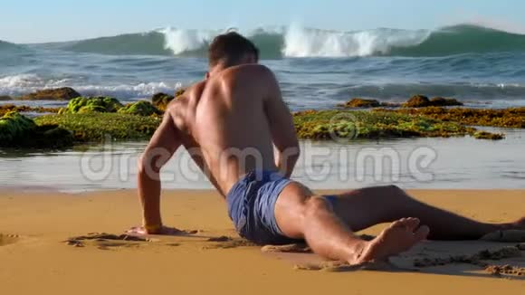 穿短裤的壮汉坐在湿黄的沙滩上伸展身体视频的预览图