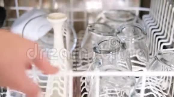 特写白种人女人的手打开洗碗机推出白色顶部篮子干净后的透明玻璃器皿视频的预览图