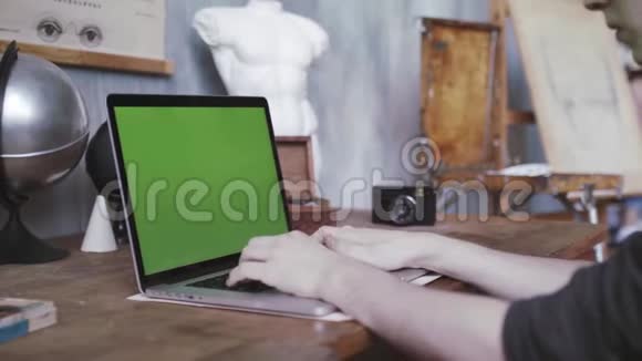 一个穿着黑色衬衫的男人坐在旧桌子旁用绿色的彩色钥匙屏幕在笔记本电脑上打字库存数据视频的预览图