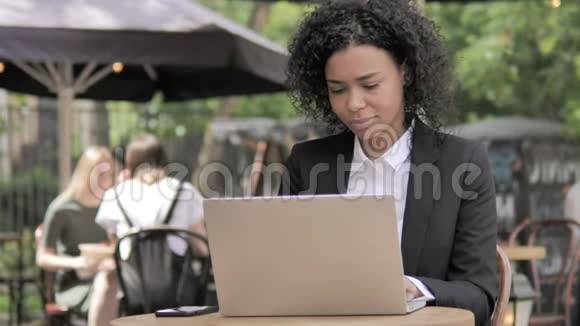 非洲女商人在户外咖啡厅的笔记本电脑上庆祝视频的预览图