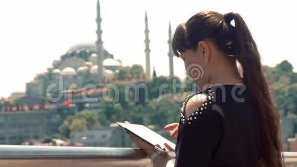 一个亚洲女孩站在城市美丽的风景旁边看着她的平板电脑视频的预览图