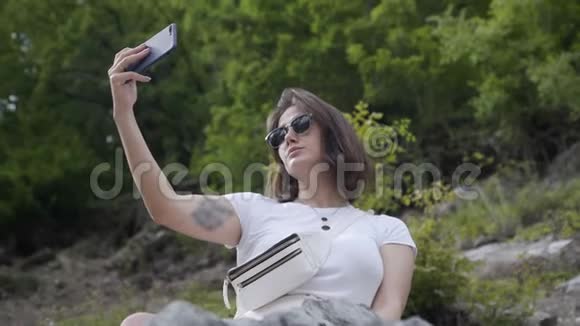 年轻的成年女游客把自拍带到山上的岩石上视频的预览图