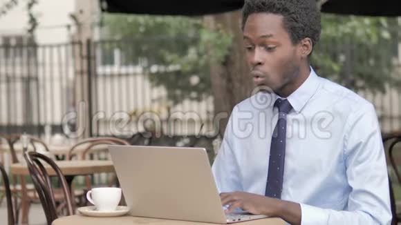非洲商人在户外咖啡厅的笔记本电脑上庆祝视频的预览图
