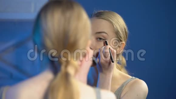漂亮的少女在镜子前涂眼线学习化妆视频的预览图