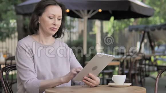 老女人坐在户外通过平板电脑成功的网上购物视频的预览图