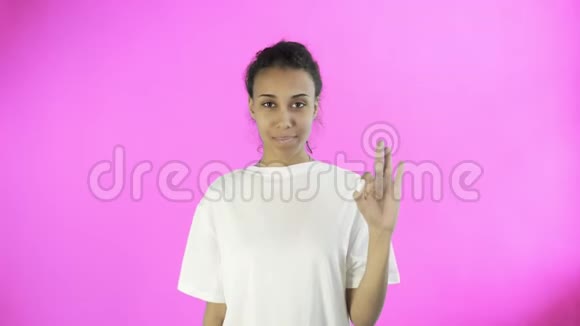 可爱的非裔美国女孩在工作室的粉色背景上用两个拇指和微笑表现得很好视频的预览图