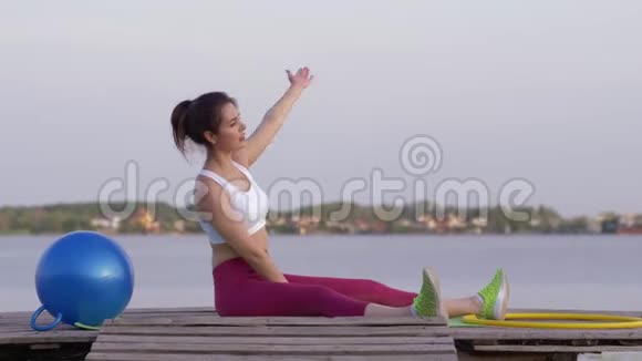 在户外的木桥上进行运动锻炼时年轻的健身妇女在身体向两侧倾斜时做伸展运动视频的预览图
