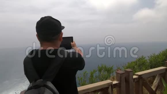 一位背着背包的游客站在一座木桥附近观看美丽的大海视频的预览图