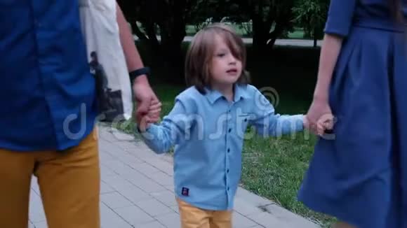 快乐的小男孩走着牵着父母的手紧紧地视频的预览图