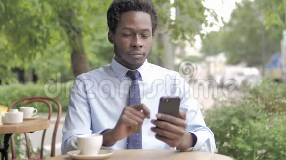 非洲商人坐在户外咖啡厅在智能手机上失声喧哗视频的预览图