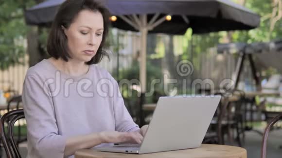 带头痛的老女人用笔记本电脑坐在户外视频的预览图