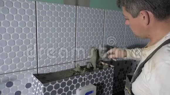 男工在壁橱框架上涂上粘合剂并安装瓷砖视频的预览图