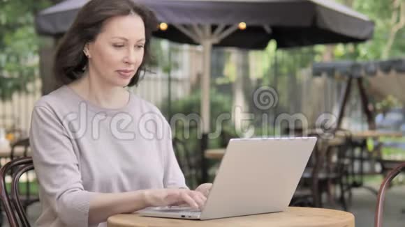老女人通过笔记本电脑聊天坐在户外咖啡厅视频的预览图