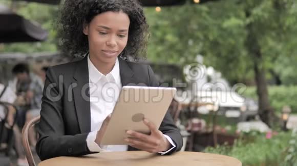 非洲妇女使用平板电脑坐在室外咖啡厅视频的预览图