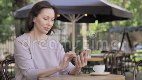 坐在户外咖啡厅的智能手机上的老女人追求成功视频的预览图