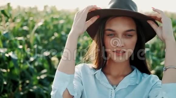 戴着帽子的漂亮女孩站在玉米地微笑着在夕阳下看着相机的肖像女孩戴帽子视频的预览图