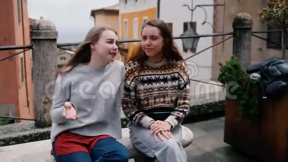 两个年轻的女人坐在长凳上说话其中一个展示给另一个视频的预览图