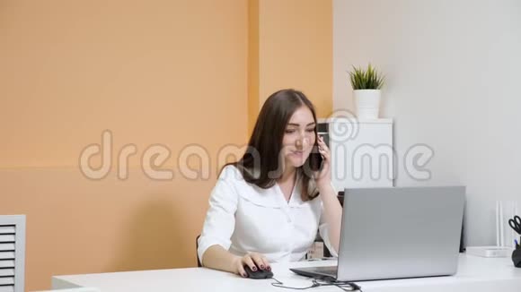 微笑的女接待员在笔记本电脑上谈论智能手机视频的预览图