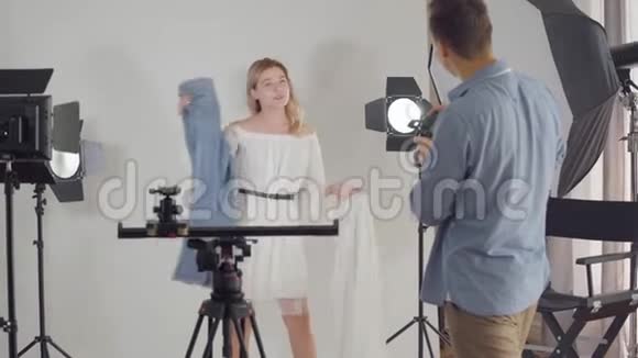 拍摄的后台摄影师在摄影棚里拍可爱的女孩在白色背景上摆姿势的照片时尚视频的预览图