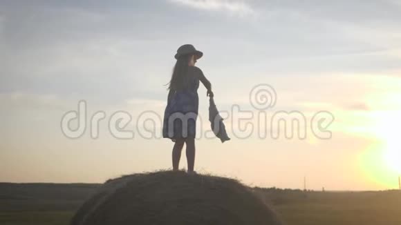 日落时干草跳跃的小女孩在乡下的干草堆附近的女孩视频的预览图