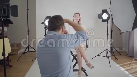 著名的男摄影师为坐在白色背景椅子上的迷人优雅的女人拍照视频的预览图