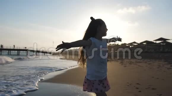 美丽快乐的小女孩剪影在日落海滩上享受大自然的户外举手快乐快乐视频的预览图